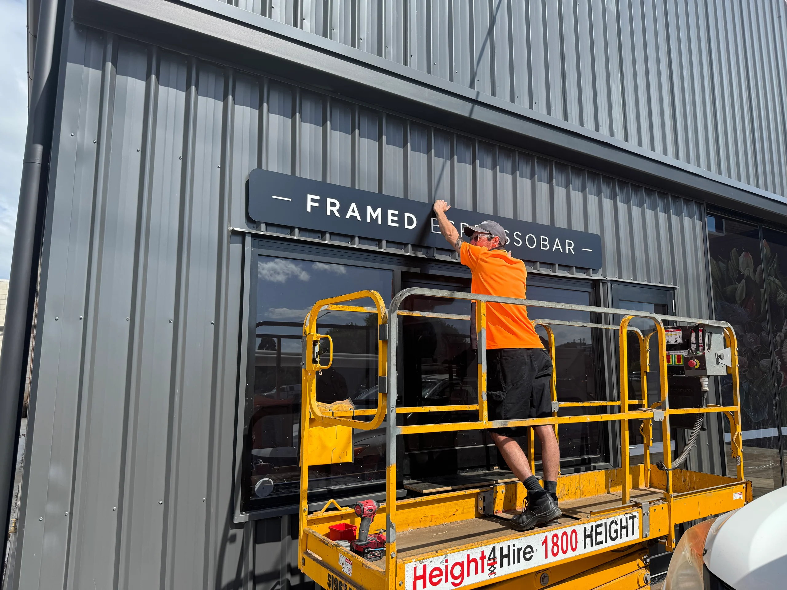 ALE installer on an elevated work platform fitting the Framed Espresso Bar sign