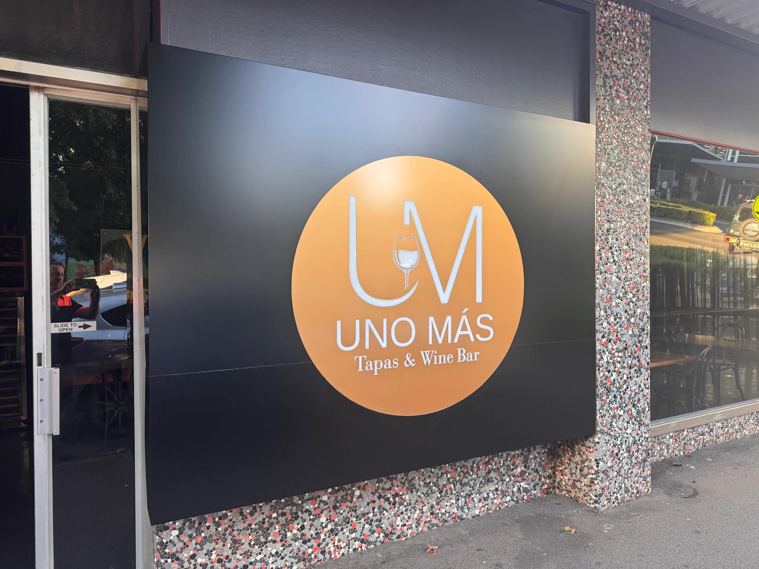 Uno Más Tapas & Wine Bar logo sign on a black feature wall
