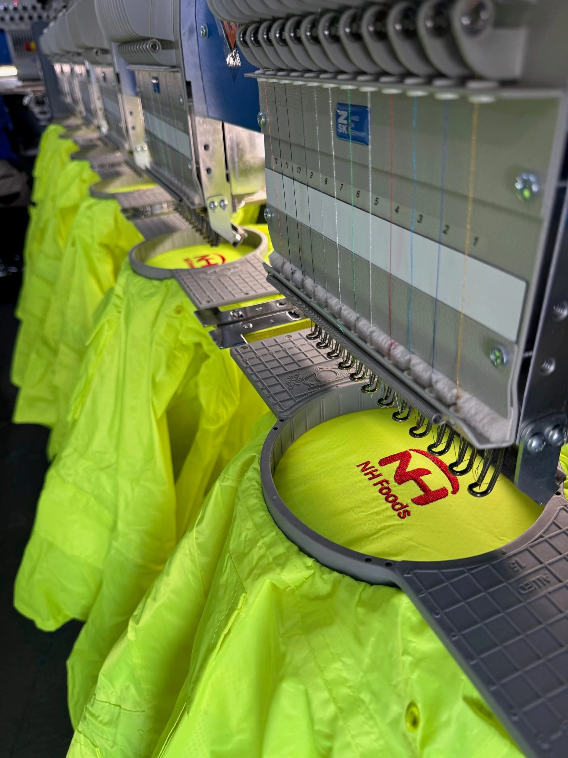 Multi-head embroidery machine stitching logos onto hi-vis shirts